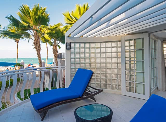 A balcony featuring blue chairs overlooks a serene ocean view under a clear sky.