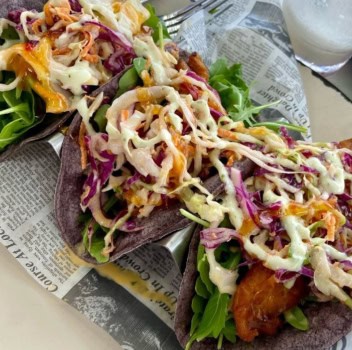 Three tacos topped with coleslaw and dressing, served on a sheet of newspaper.