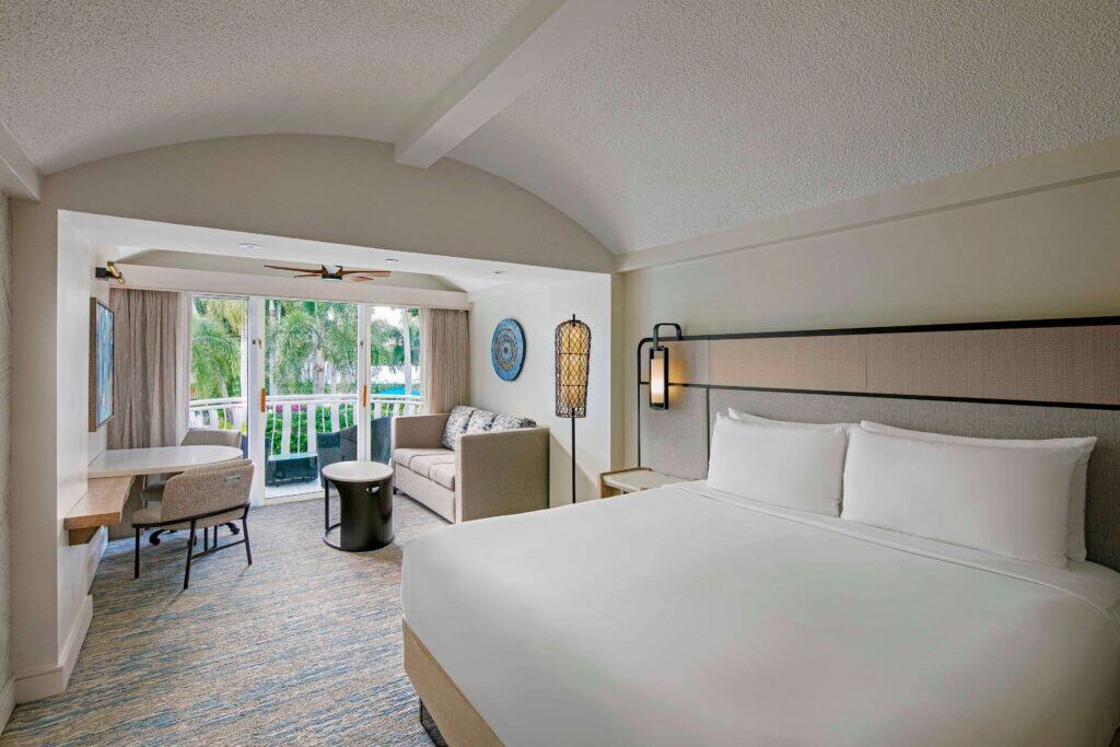 A hotel room featuring a king bed and a flat-screen television against a neutral-colored wall.