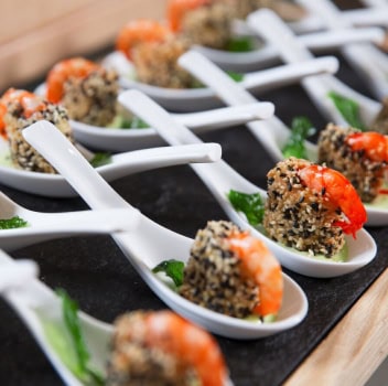 A decorative tray featuring shrimp and colorful vegetables served on individual spoons for a gourmet presentation.