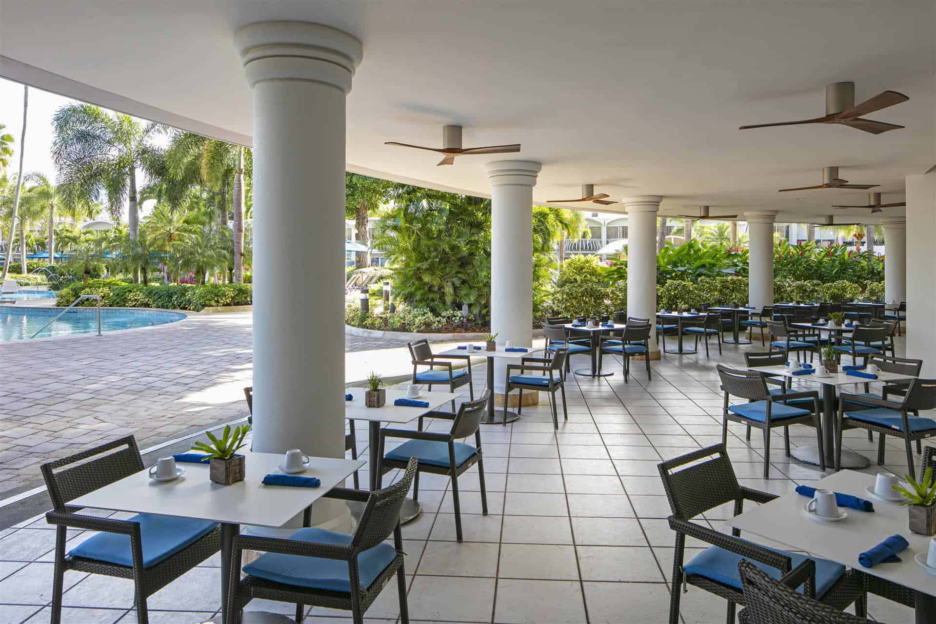 A restaurant patio featuring tables and chairs overlooking a serene pool area.