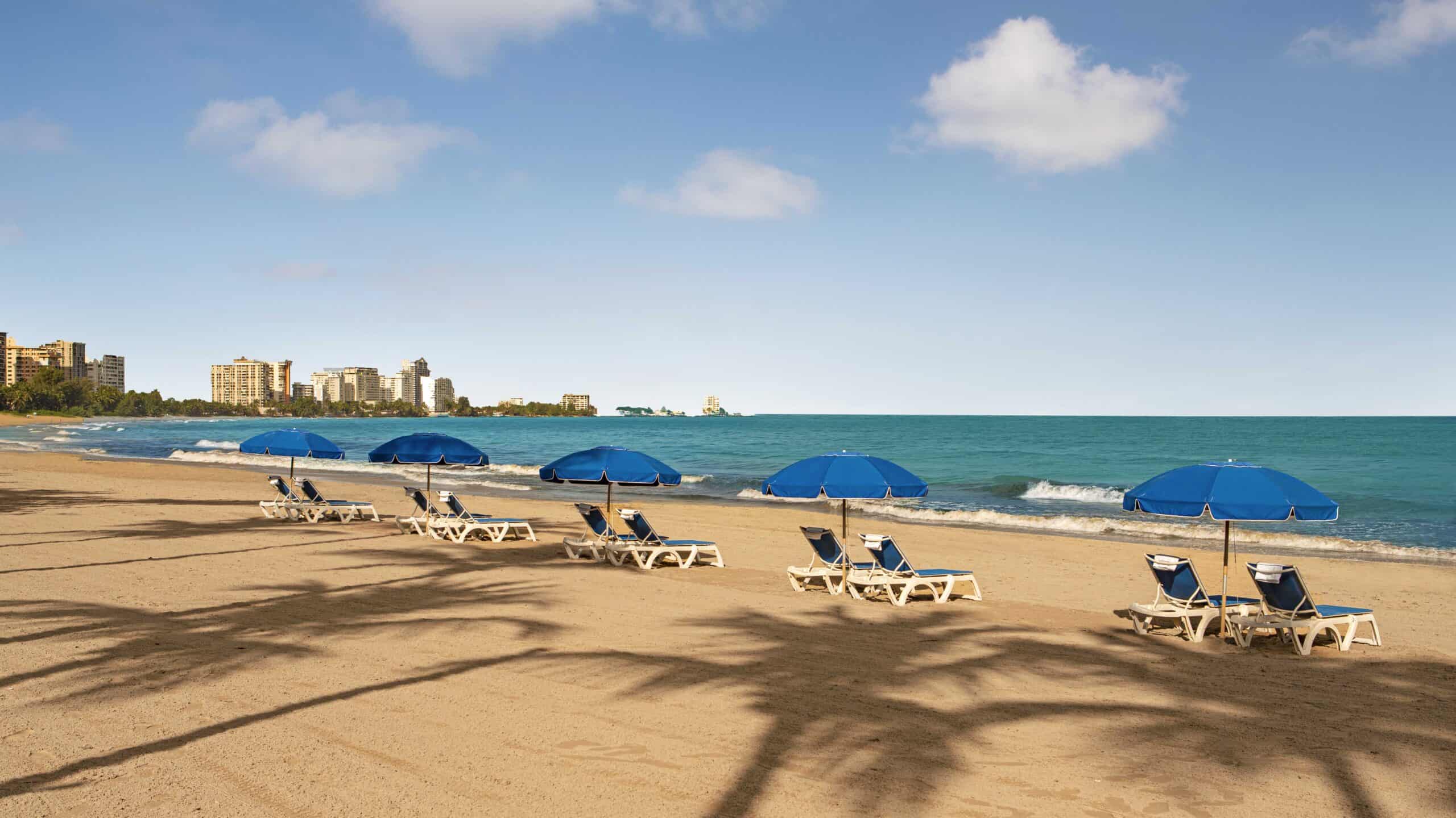 A sunny beach scene featuring colorful chairs and umbrellas set up on the soft sand.