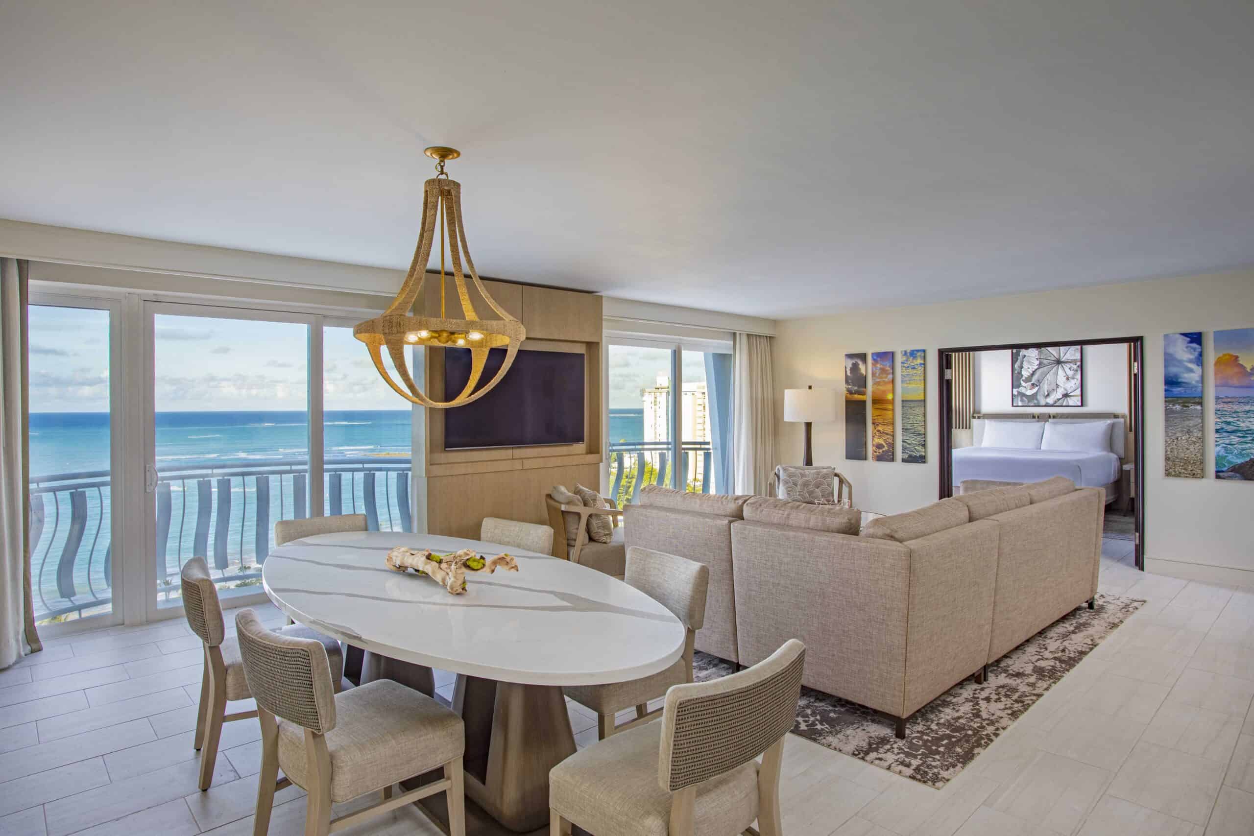 Ocean view living and dining room at a resort, featuring large windows overlooking the sea and stylish furnishings.