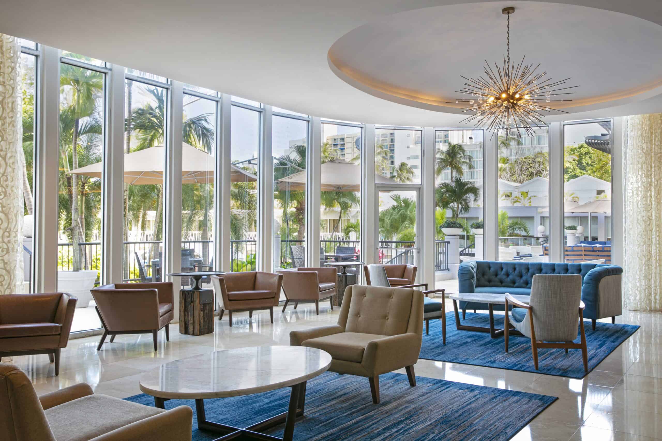 Hotel lobby featuring large windows and an elegant chandelier hanging from the ceiling, creating a bright atmosphere.