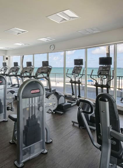 A gym featuring various exercise equipment with large windows showcasing a scenic view of the ocean.
