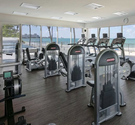 A gym room featuring exercise equipment and large windows showcasing a scenic view of the ocean.
