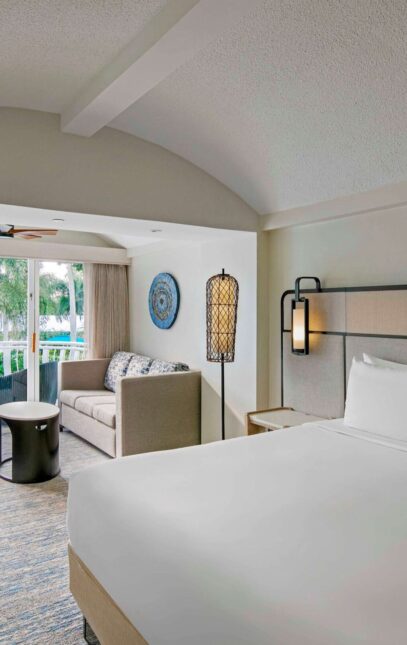 A hotel room featuring a king bed and a flat-screen television against a neutral-colored wall.