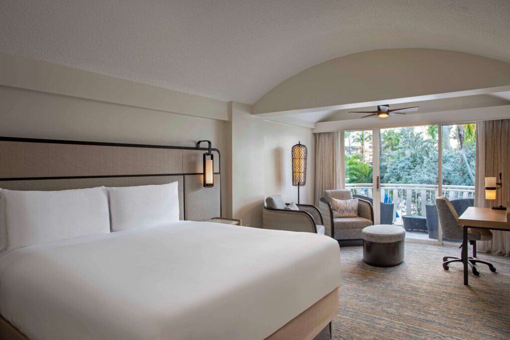 A hotel room featuring a king bed and a balcony with outdoor seating, offering a view of the surroundings.