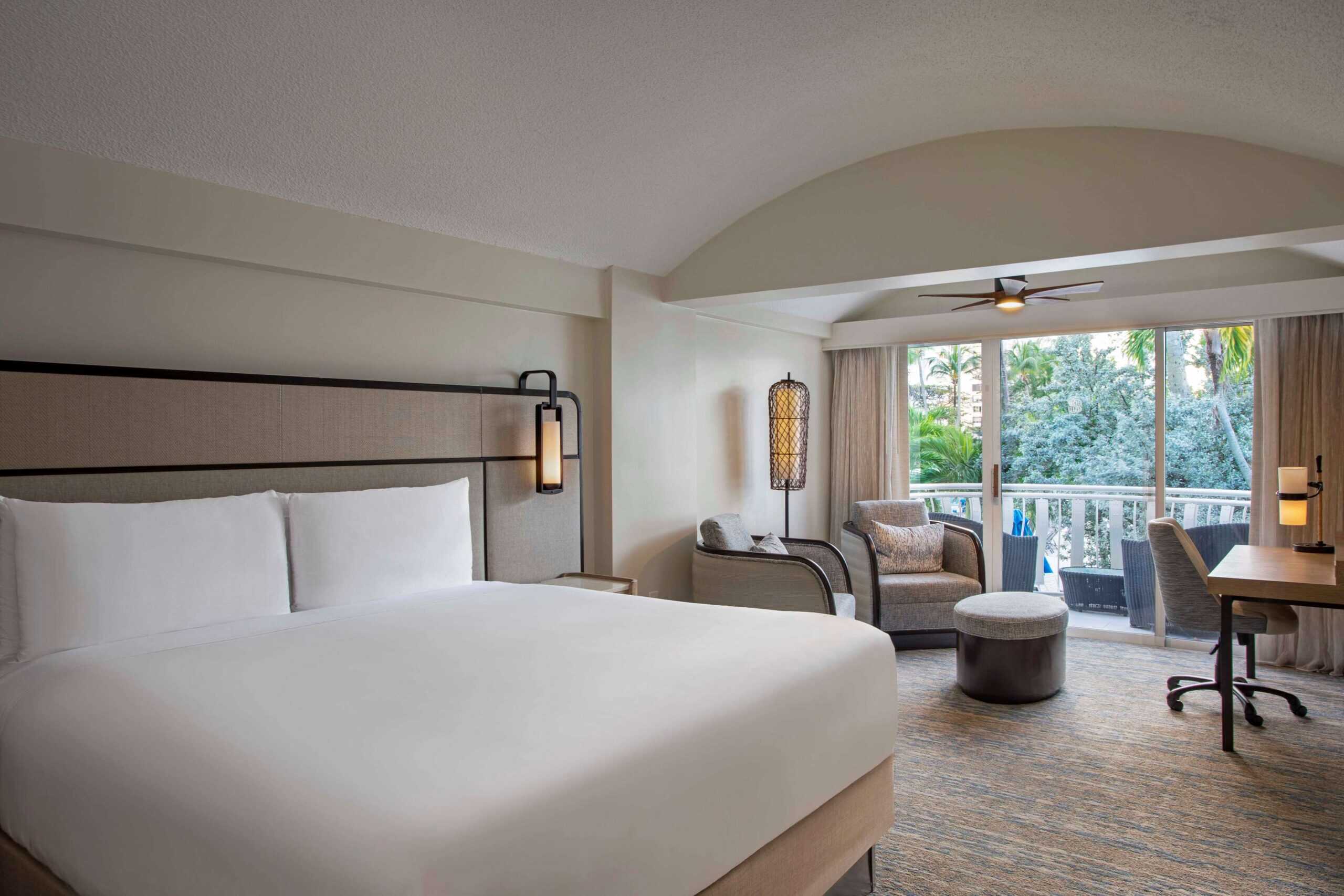 A hotel room featuring a king bed and a balcony with outdoor seating, offering a view of the surroundings.