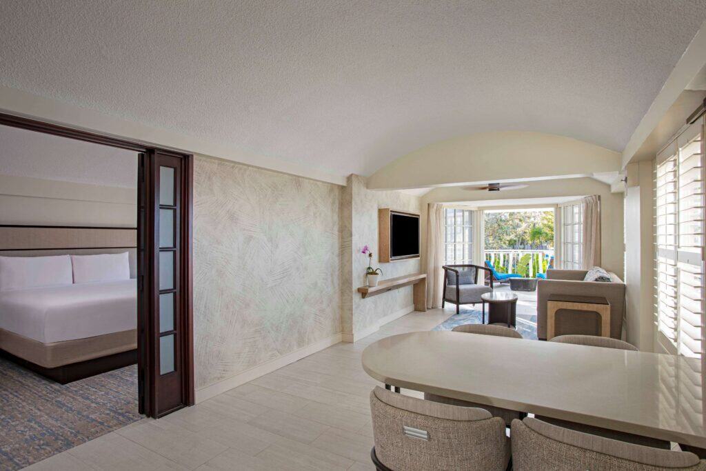 A hotel room featuring a bed, a television, and a balcony with natural light streaming in.