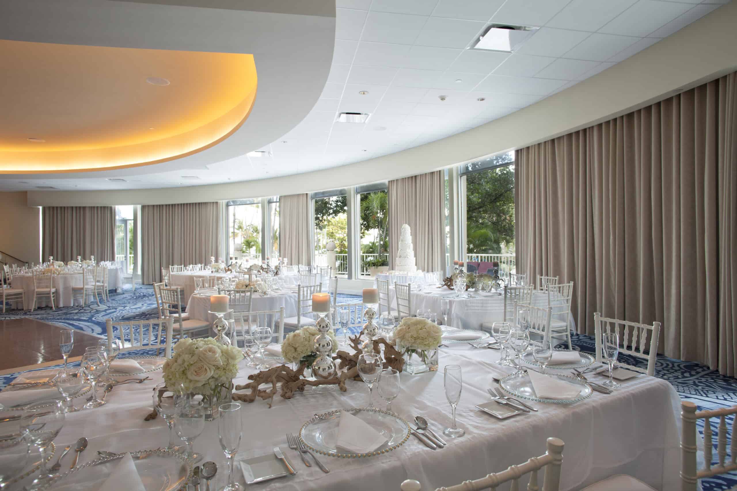 A spacious wedding reception featuring white linens and a large window, creating an elegant and bright atmosphere.
