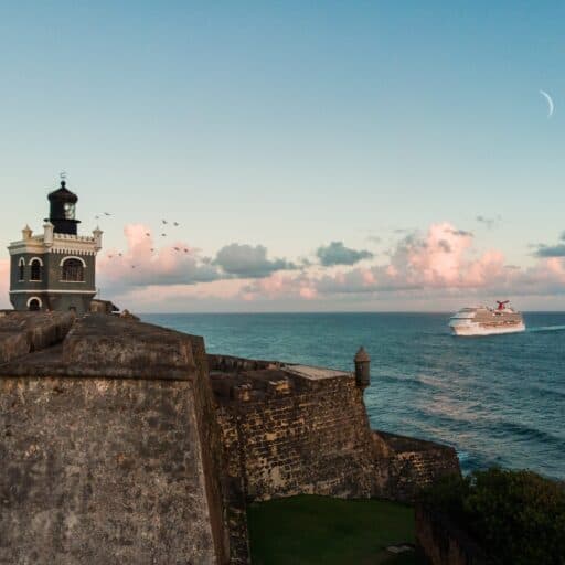 A cruise ship passes by the historic fort in San Juan, Puerto Rico, with the ocean and sky in the background.