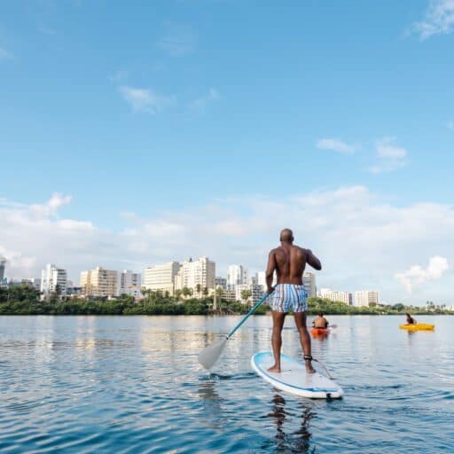 A man paddles a stand-up paddle board on calm water, enjoying a sunny day outdoors.