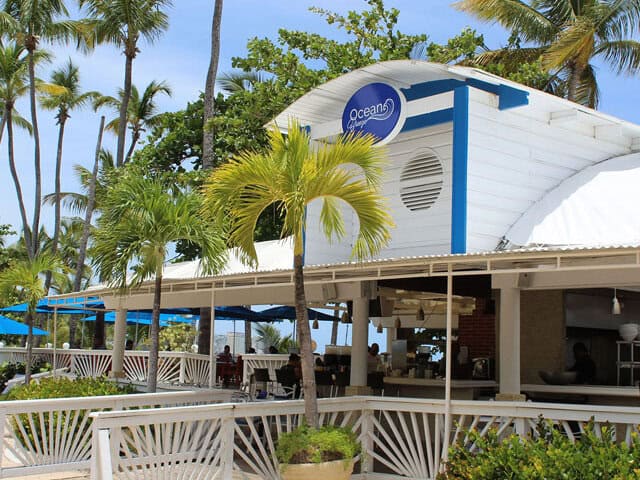 A restaurant featuring a white roof and blue umbrellas, set in a vibrant outdoor dining area.