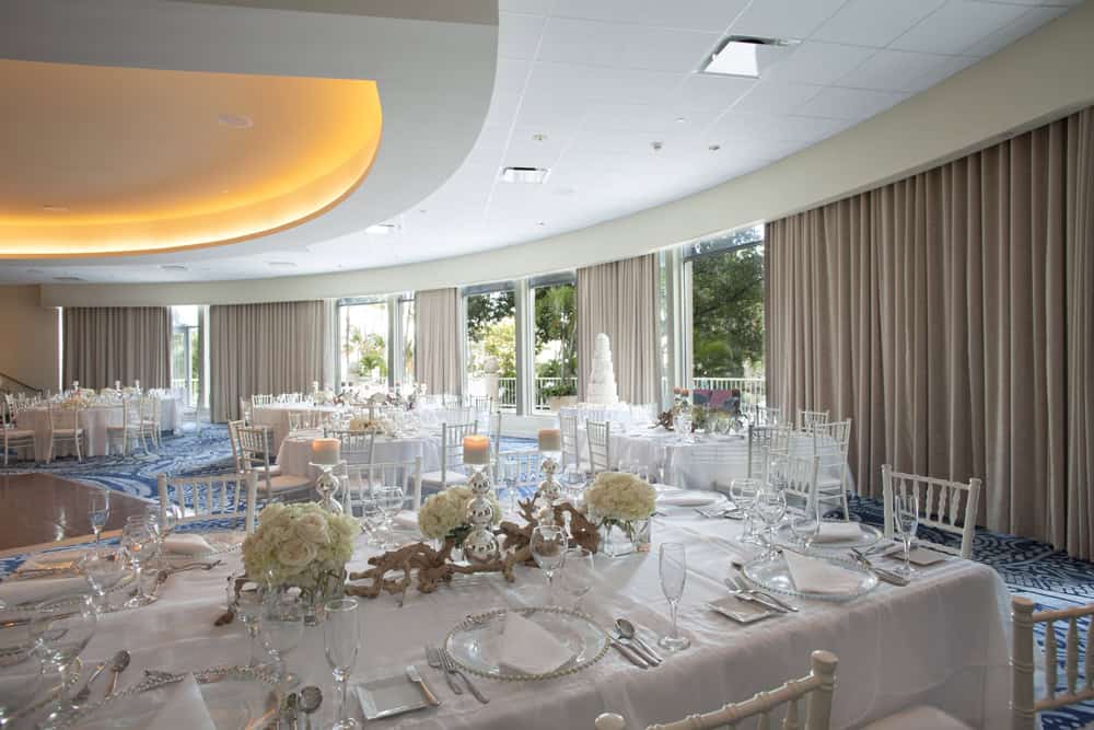 A spacious wedding reception featuring white linens and a large window, creating an elegant and bright atmosphere.