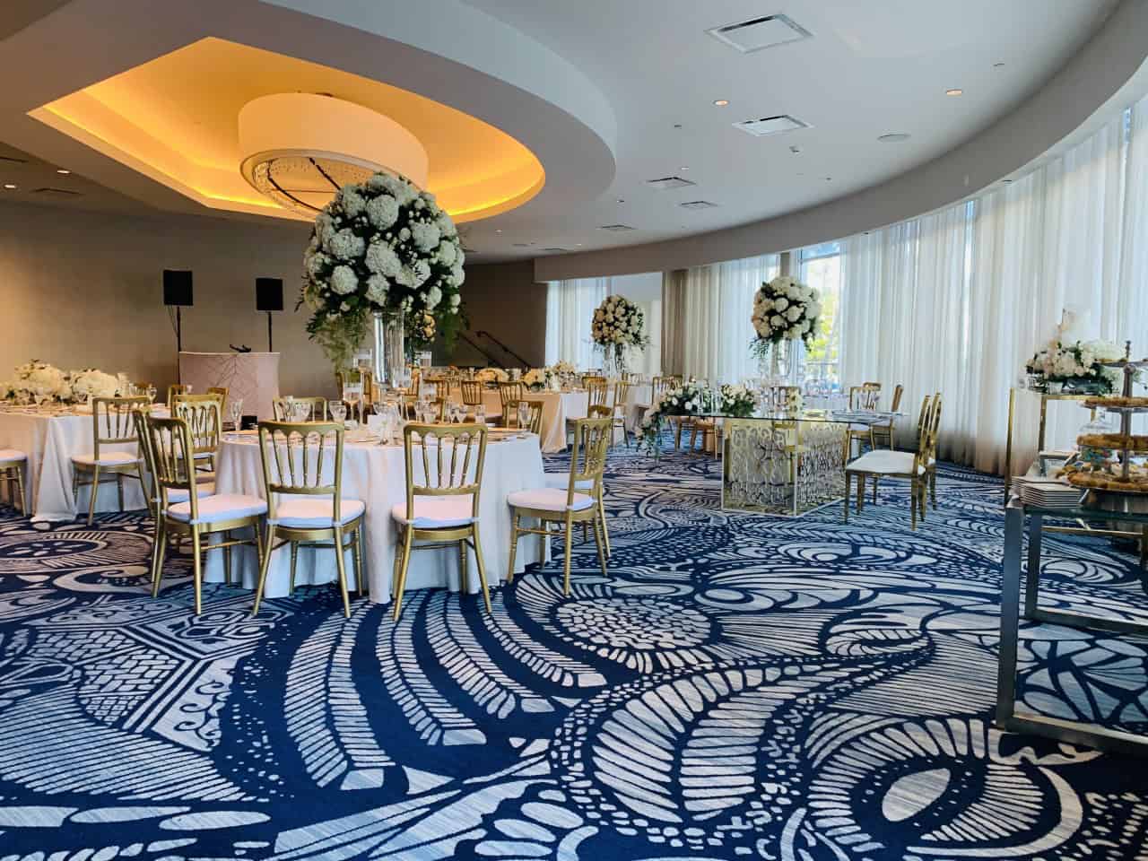 A wedding reception room featuring blue carpet and elegant gold chairs arranged for guests.