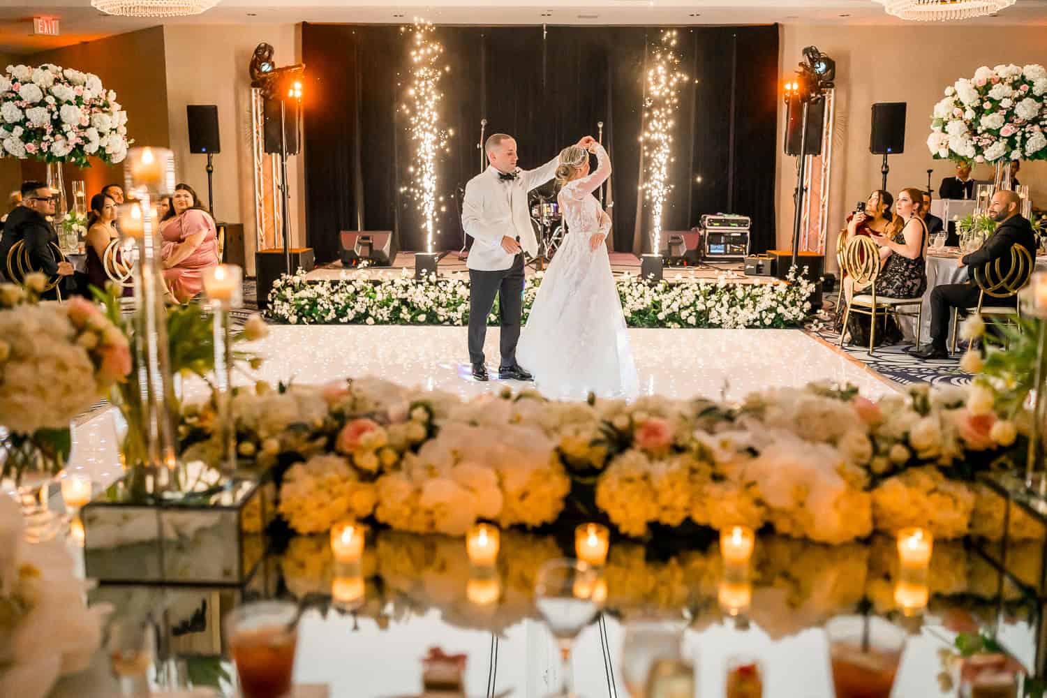 A bride and groom share their first dance, surrounded by soft lighting and joyful guests at their wedding reception.