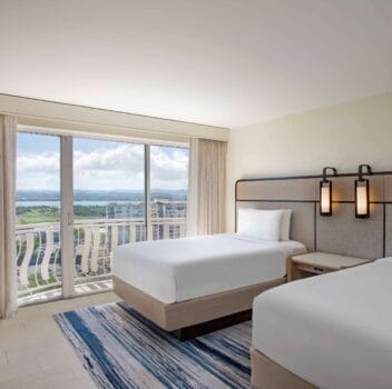 Two beds in a hotel room with a scenic view of the ocean visible through large windows.