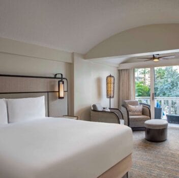 A hotel room featuring a king bed and a flat-screen television against a neutral-colored wall.