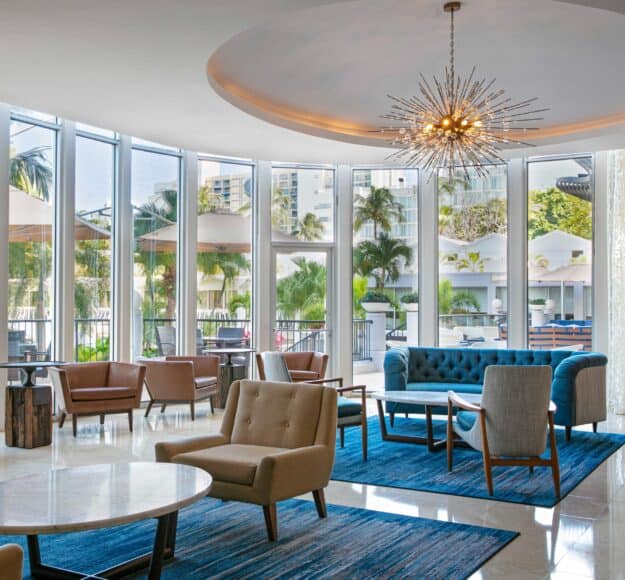 Hotel lobby featuring large windows and an elegant chandelier hanging from the ceiling, creating a bright atmosphere.