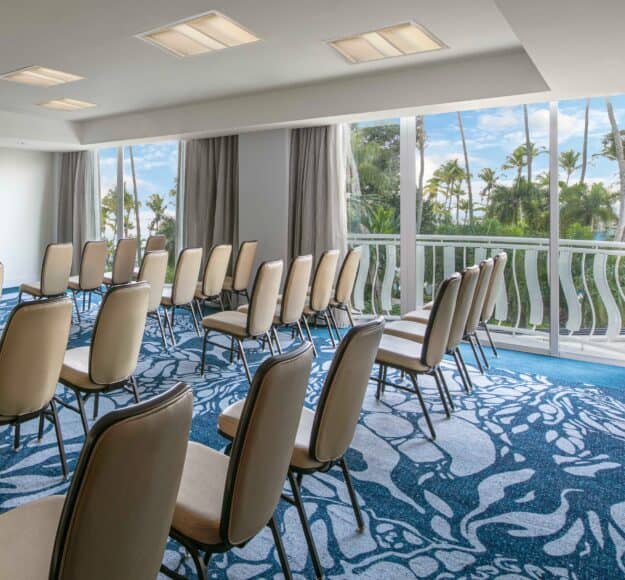 A conference room featuring chairs arranged around a table, with large windows offering a view of the ocean.